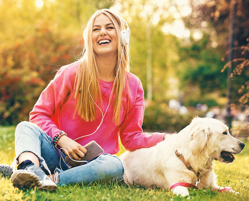 frau hoert musik mit hund auf wiese